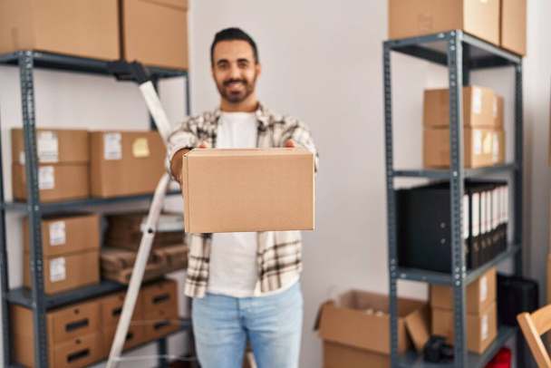 Young hispanic man ecommerce business worker holding package standing at office - Photo, Image