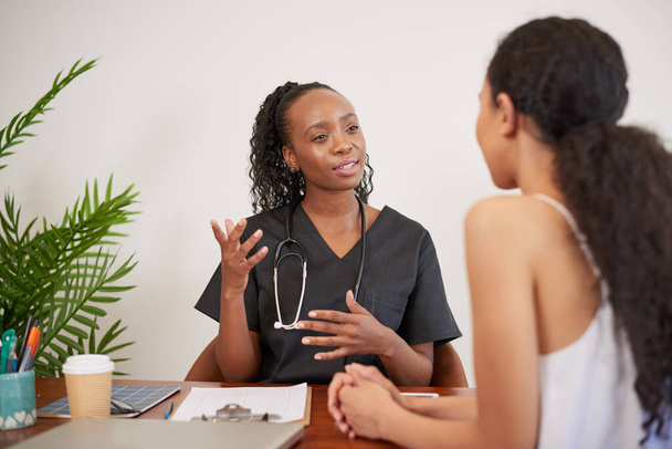 Откровенный снимок чёрной женщины-врача, объясняющей пациентке во время консультации врача. Высокое качество фото - Фото, изображение