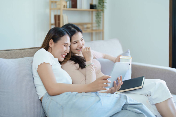 lgbtq, концепція lgbt, гомосексуальність, портрет двох азіатських жінок, які позують щасливими разом і люблять один одного, граючи планшет на дивані
. - Фото, зображення