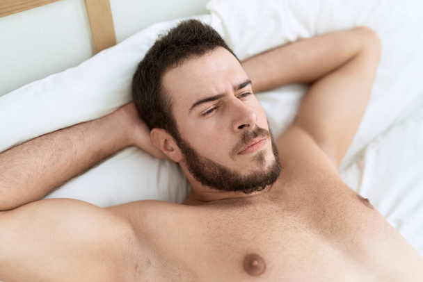 Junger hispanischer Mann liegt mit entspanntem Gesichtsausdruck im Schlafzimmer im Bett - Foto, Bild