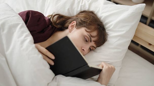 Молода біла жінка читає книгу в ліжку в спальні
 - Фото, зображення