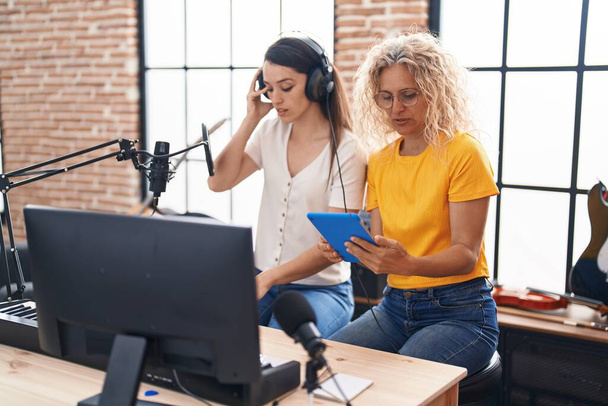 Müzik stüdyosunda klavye ve touchpad kullanarak şarkı besteleyen iki kadın müzisyen. - Fotoğraf, Görsel