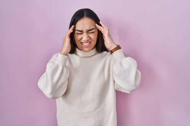 Молодая южно-азиатская женщина стоит на розовом фоне с рукой на голове, головная боль, потому что стресс. страдает мигренью.  - Фото, изображение