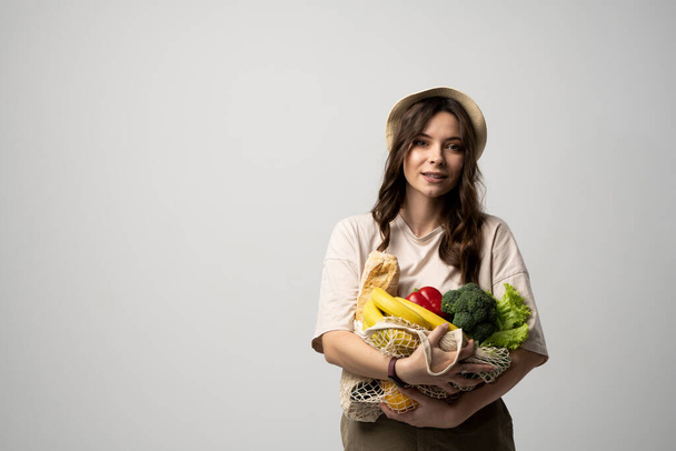 Zero waste concept. Young brunette woman holding reusable cotton shopping mesh bag with organic groceries from a market. Concept of no plastic. Zero waste, plastic free. Sustainable lifestyle - Foto, imagen