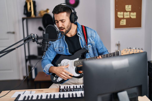 Giovane uomo ispanico cantare canzone suonare la chitarra elettrica in studio di musica - Foto, immagini