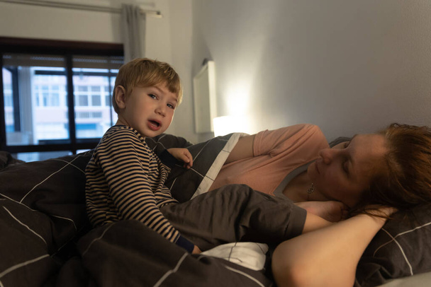 Um menino e sua mãe estão deitados na cama. A meio do tiro - Foto, Imagem