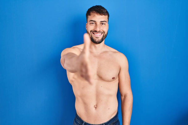 Handsome hispanic man standing shirtless smiling friendly offering handshake as greeting and welcoming. successful business.  - Fotografie, Obrázek