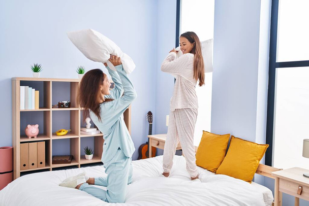 Жінка і дівчина мати і дочка борються з подушкою на ліжку в спальні
 - Фото, зображення