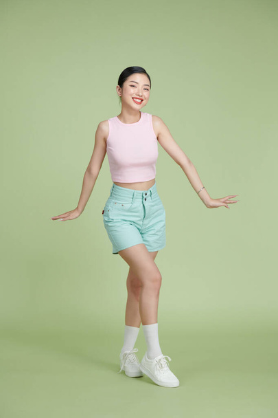 Corpo inteiro de menina feliz dançando suas mãos para cima no fundo pastel verde - Foto, Imagem