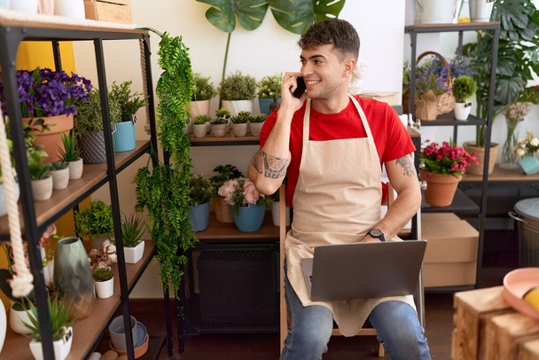 Young hispanic man florist talking on smartphone using laptop at flower shop - Valokuva, kuva
