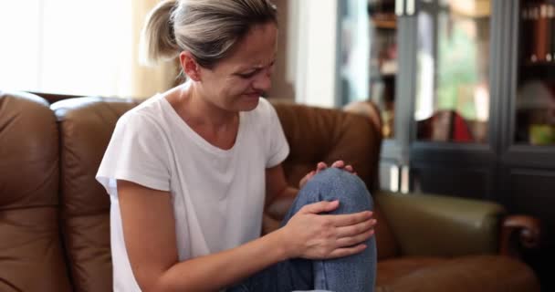 ブロンドの女性マッサージは、自宅でソファに座って痛みを和らげるために手で膝を痛めます。主婦ありますに苦しんでいます急性痛みを追求唇遅い動き - 映像、動画
