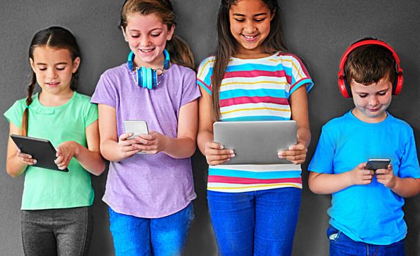 The smartest generation around. Studio shot of a group of kids using wireless technology against a gray background - Foto, immagini