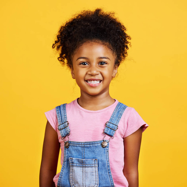 Studio portrait mixed race girl looking standing alone isolated against a yellow background. Cute hispanic child posing inside. Happy and cute kid smiling and looking carefree in casual clothes. - Foto, Imagem