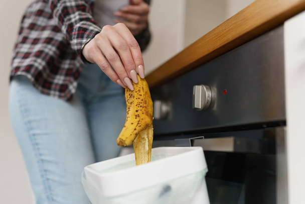 Woman throwing banana pill in a bokashi bin for compost. Female person recycling organic food waste in a composting container - Zdjęcie, obraz