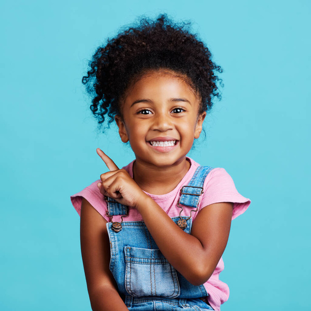 Portrait, pointing and mockup with a girl on a blue background in studio showing product placement space. Kids, marketing and advertising with an adorable female child indoor to point at branding. - Photo, Image