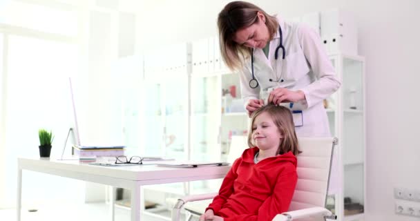 Ystävällisesti lääkäri tutkii pienen tytön hiukset punkkien klinikalla hidastettuna. Hoitaja etsii loisia lapsen päähän. Säännöllinen lääkärintarkastus sairaalassa - Materiaali, video