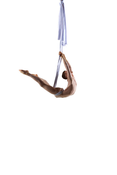 Flexible, athletic male aerial gymnast training with aerial silk ribbons against white studio background. Strong body. Concept of art, sportive lifestyle, hobby, action and motion, beauty - Фото, изображение