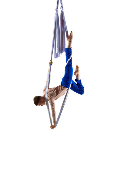 Strong, athletic, young man, professional aerial gymnast training with aerial silk ribbons against white studio background. Concept of art, sportive lifestyle, hobby, action and motion, beauty - Photo, Image