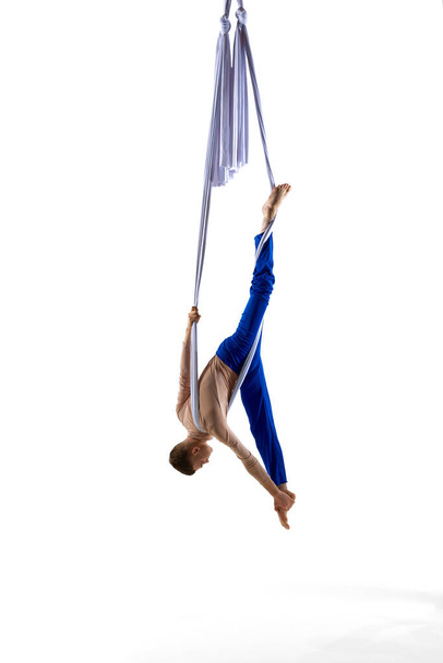 Professional male acrobat, aerial gymnast training with aerial ribbons, doing tricks against white studio background. Concept of art, sportive lifestyle, hobby, action and motion, beauty, gymnastics - Photo, image
