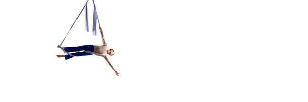 Dynamic image of young man, professional aerial gymnast, acrobat training with aerial tissue against white background. Concept of art, sportive lifestyle, action and motion. Banner. Copy space for ad - Foto, Imagem