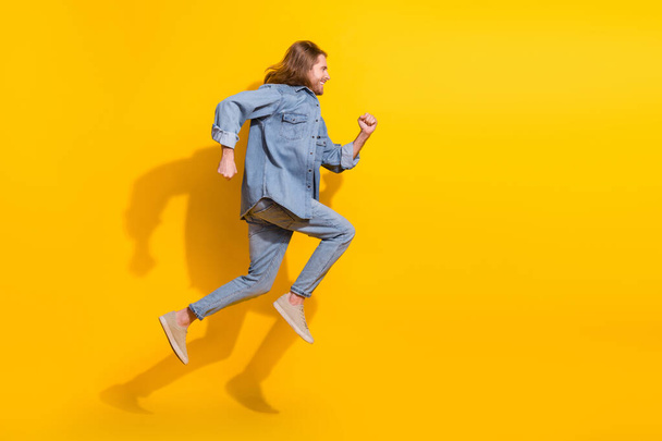 Full length photo of funky cool guy dressed jeans shirt jumping high running emtpy space isolated yellow color background. - Foto, imagen