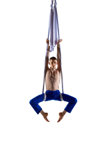 Young man, professional aerial acrobat, gymnast training on aerial ribbons against white studio background. In air. Concept of art, sportive lifestyle, hobby, action and motion, beauty - Fotoğraf, Görsel