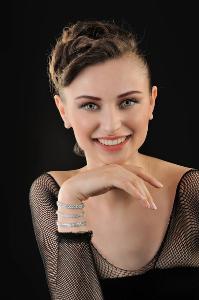 portrait of beautiful young woman in black fishnet dress with diamont bracelet on black background - 写真・画像