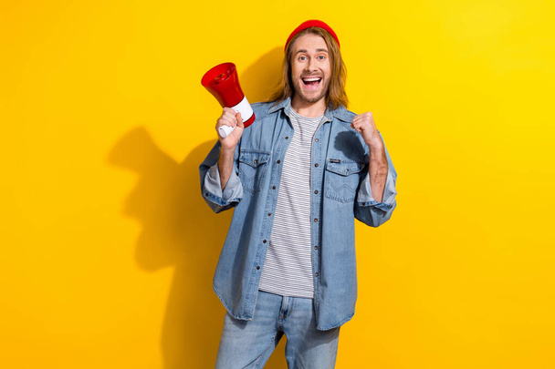 Photo of impressed satisfied guy with long hairdo dressed jeans shirt hold megaphone shouting yes isolated on yellow color background. - Fotoğraf, Görsel