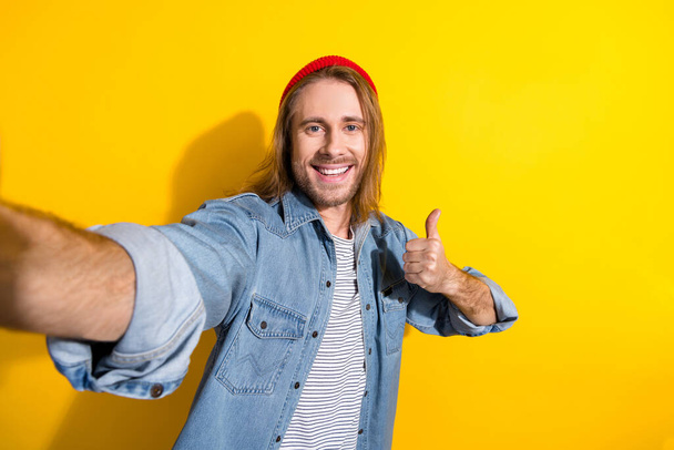 Photo of positive cool man wear denim jacket showing thumb up tacking selfie isolated yellow color background. - Foto, imagen