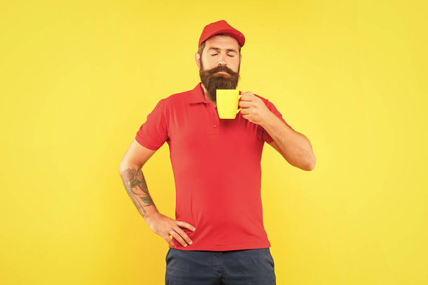 Serious bearded man smelling hot beverage with closed eyes holding cup yellow background, coffee. - Фото, зображення