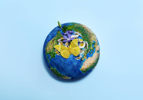 Earth globe with flowers and butterfly on light blue background - Foto, Imagen