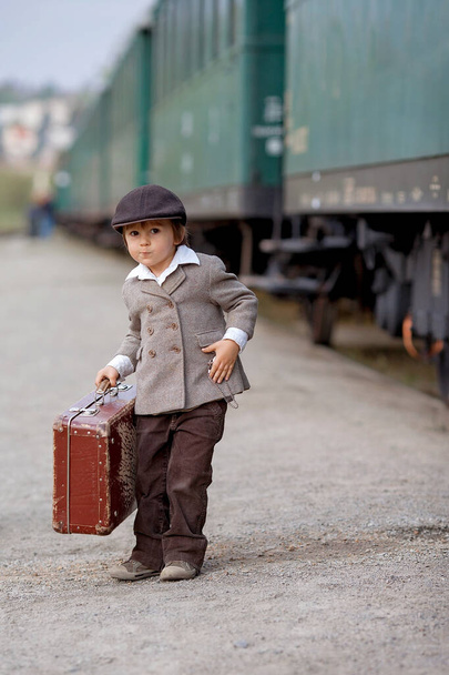 Two boys, dressed in vintage clothing and hat, with suitcase, on a railway station - Photo, image