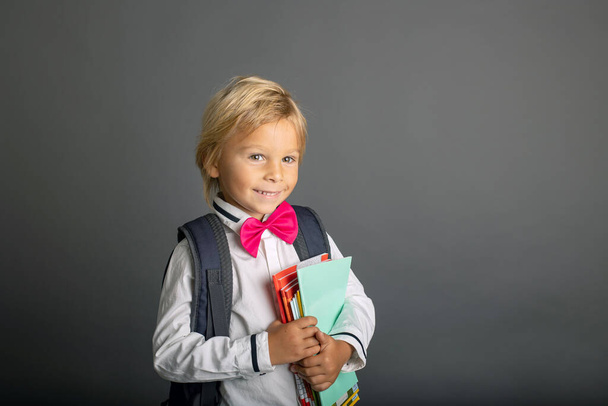 Cute preschool blond child, boy, holding books and notebook, apple, wearing glasses, ready to go to school - Фото, изображение
