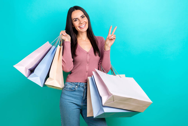 Portrait picture of youngster shopaholic lady show v-sign hello symbol hold shop bags enjoy packages purchase isolated on cyan color background. - Foto, immagini