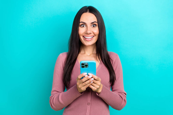 Портрет молодої збудженої смішної жінки брюнетки Блузка для волосся тримає смартфон, переглядаючи відео YouTube в тенденціях, ізольованих на фоні синього кольору
. - Фото, зображення