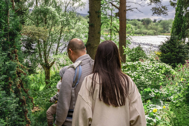 Egy multikulturális család sétál a természetben az erdőben a Dr. Neil 's Gardenben. Az apa egy babahordozónál hordja a fiát. Többnemzetiségű és kétnemzetiségű brit család. - Fotó, kép