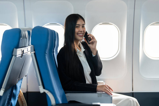 Joven empresaria exitosa que trabaja hablando por teléfono móvil mientras está sentada en la cabina del avión. - Foto, Imagen