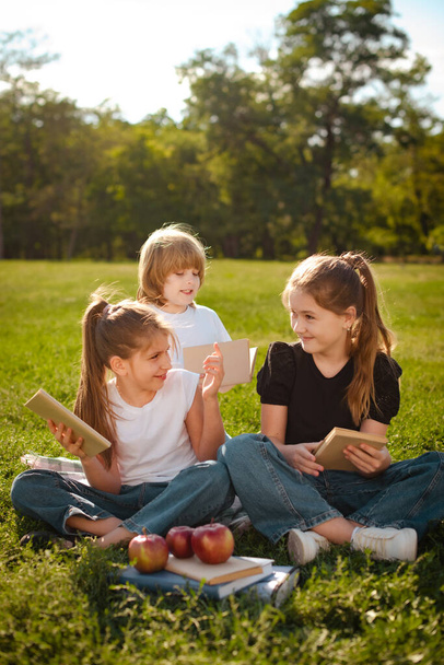niños y niñas en el parque sentado en la hierba verde después de las clases de la escuela - Foto, Imagen