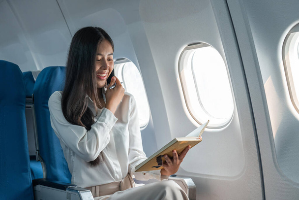 Biznes młody Azji kobieta mówi przez telefon podczas dla danych raport finansowy w samolocie. - Zdjęcie, obraz
