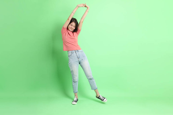 The young adult Asian woman with casual clothes with jeans standing on the green background. - Фото, изображение