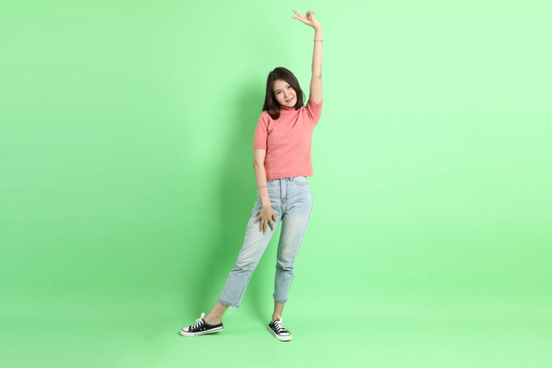 Молодая взрослая азиатка в повседневной одежде в джинсах, стоящая на зеленом фоне. - Фото, изображение