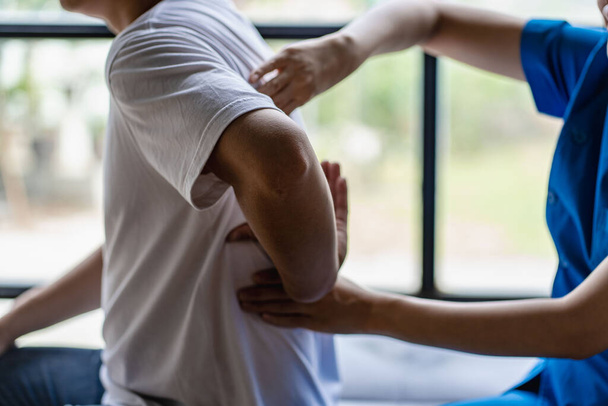Молодой азиат проводит физиотерапию и просит совета у мышечной боли с плечом, конечностями в реабилитационном центре. - Фото, изображение