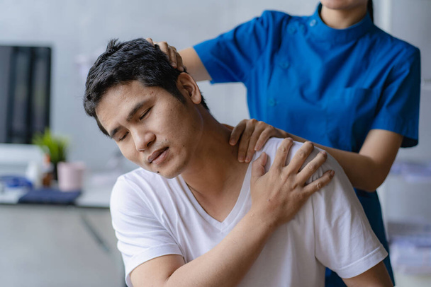Jovem asiático fazendo fisioterapia e buscando conselhos de dor muscular com ombro, membros no centro de reabilitação. - Foto, Imagem