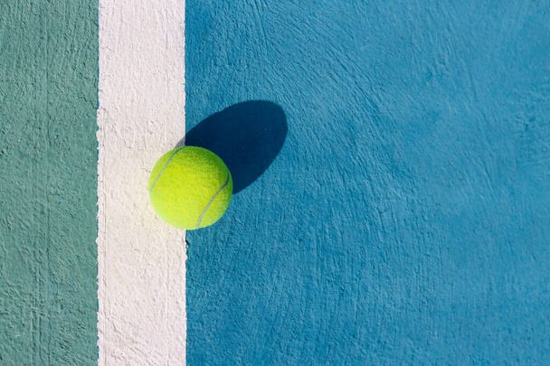 Tennis ball on a white line on hard tennis court of blue color. Flat lay, top view, copy space. Summer sport. Tennis court with a tennis ball close up. Summer activities and active life concept - Photo, Image