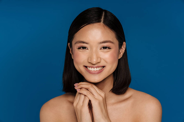 Asian half-naked woman smiling and looking at camera isolated over blue background - Foto, immagini