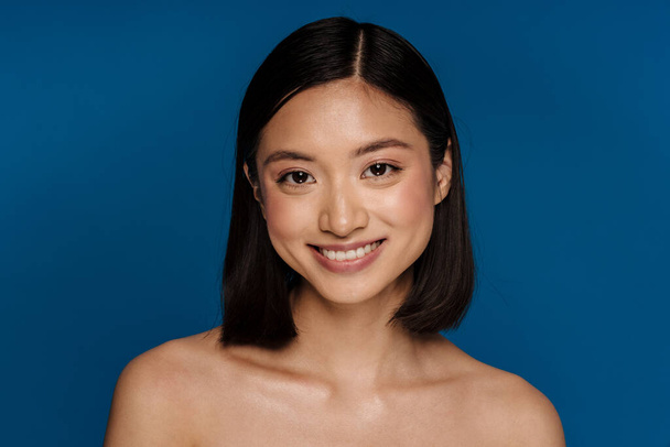 Asian half-naked woman smiling and looking at camera isolated over blue background - Photo, Image