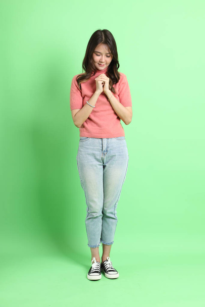 The young adult Asian woman with casual clothes with jeans standing on the green background. - Photo, image