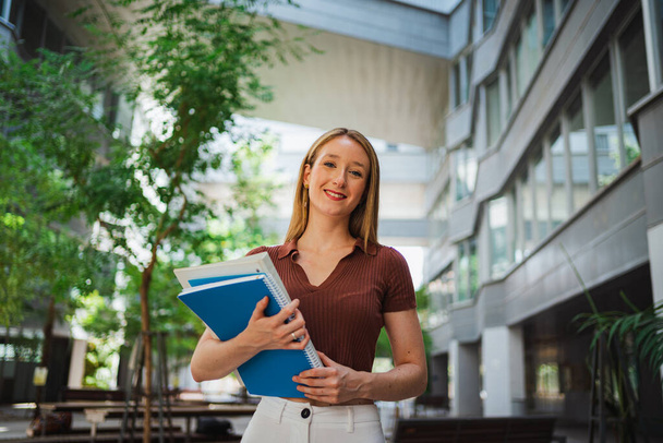 Portrait d'une jeune étudiante souriante tenant des cahiers et des dossiers. Elle est à l'université.. - Photo, image
