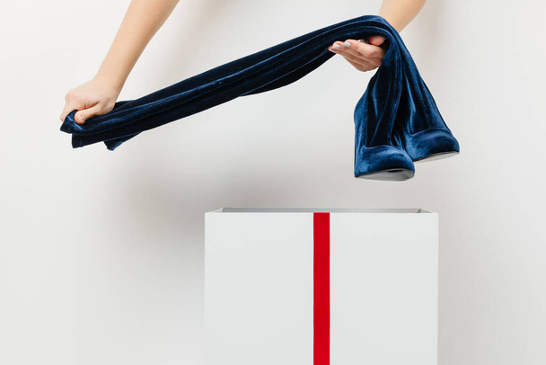 hermosas manos femeninas ponen botas azules en una caja blanca con una cinta roja sobre un fondo blanco aislado. concepto de regalo, sorpresa - Foto, imagen