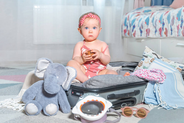 Bébé fille caucasienne en valise de voyage. Enfant à l'intérieur des bagages emballés pour des vacances pleines de vêtements, d'enfants et de préparation de voyage en famille - Photo, image